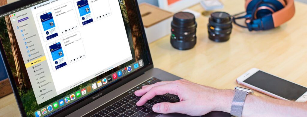 A person's hands are visible on a MacBook Pro keyboard, with the laptop screen displaying the Mail Designer 365 "TeamCloud" interface. The screen shows multiple email newsletter designs, illustrating how Team Cloud enables all users in a team to access and edit the team's templates collaboratively. Headphones and camera lenses are blurred in the background.